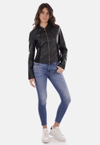 Giubbotto in pelle nera con un design aderente, chiusura con zip e pannelli testurizzati, abbinato a jeans skinny azzurri e sneakers bianche.