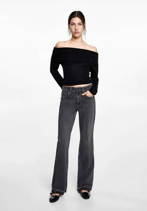 Schwarzes, schulterfreies Langarmoberteil, kombiniert mit grauen, flared Jeans. Das Oberteil sitzt eng an, die Jeans haben einen klassischen Schnitt mit vorderen Taschen.