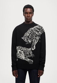 Maglione nero con un design lavorato a maglia di due leopardi bianchi, scollatura rotonda e polsini a coste, realizzato in materiale morbido e testurizzato.