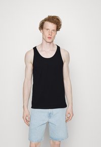 Débardeur en coton noir avec un col rond, associé à un short en denim bleu clair à coupe décontractée et à ourlet effiloché.