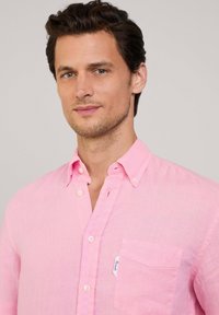Camisa de botones de color rosa claro hecha de lino. Cuenta con un bolsillo en el pecho y una pequeña etiqueta. Diseño casual con un corte holgado.