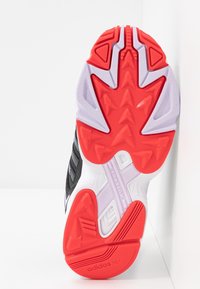 Black athletic shoe sole with red, white, and lavender accents. Features textured rubber for grip and a distinct tread pattern for traction.