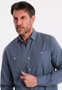 Blaues Langarmhemd aus weichem Stoff, mit einem Button-Down-Kragen, zwei vorderen Taschen mit Knöpfen und einem lässigen Schnitt.