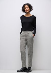 Haut noir à manches longues associé à un pantalon texturé gris clair. Le mannequin porte des chaussures noires à lacets. Design simple et ajusté avec une coupe moderne.