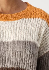 Nahaufnahme eines gestrickten Pullovers mit orangefarbenen, weißen und grauen horizontalen Streifen, der von einer Person getragen wird.