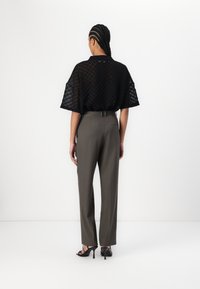 Haut noir transparent à motifs avec des manches courtes, associé à un pantalon gris taille haute à coupe droite et des sandales noires à talons.