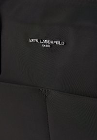 Zwarte stoffen rugzak met een opvallend zilveren logo "KARL LAGERFELD KIDS," een gladde textuur en extra stiksels aan de onderkant.