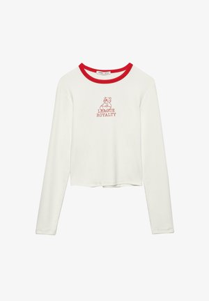 Tricou cropct cu mânecă lungă alb, cu guler roșu, având un grafic cu un urs și textul "LEAGUE ROYALTY" în roșu. Material moale și elastic.