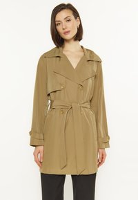 Khaki trench coat z dużym kołnierzem, na podwójne guziki i z paskiem w talii. Gładki materiał z bocznymi kieszeniami i zapinanymi rękawami.