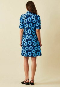 Blomstrig blå klänning med en figursydd design, korta ärmar och knälång nederkant. Har ett mönster av ljusblå och mörkblå blommor på en marin bakgrund.