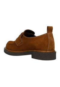 Bruine suède schoen met een ronde neus, zichtbare stiksels en een dikke zwarte rubberen zool. Beschikt over een instapdesign met een trekband aan de achterkant.