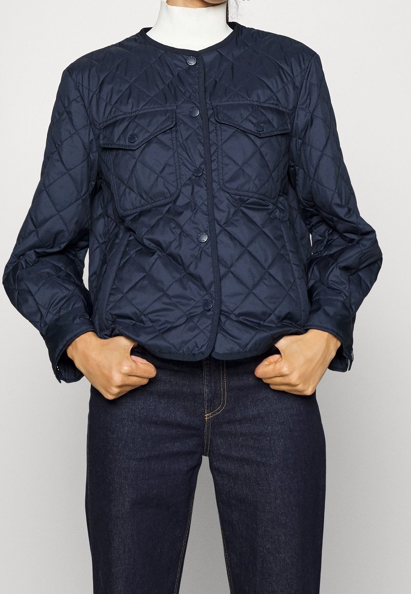 Giacca imbottita navy con colletto rotondo, bottoni a pressione sul fronte e due tasche sul petto. Tessuto liscio e design aderente.
