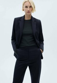 Blazer ajusté marine et pantalon assorti, fabriqués dans un tissu lisse. Comprend une coupe slim, des revers crantés et une poche poitrine.