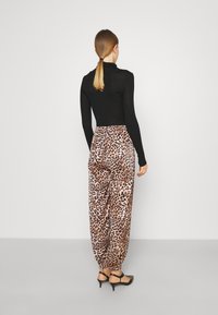 Haut noir à manches longues associé à un pantalon ample à imprimé léopard dans des tons beige et marron, avec poignets et taille élastiques.