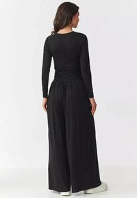 Czarna bluzka z długim rękawem z marszczeniami z tyłu, zestawiona z szerokimi czarnymi spodniami. Gładka tekstura i luźny krój.