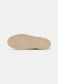 Beige gummisåle med horisontale spor og vertikale ribber for godt grep. Glatt overflate med minimale merker og rene kanter.