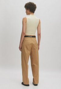 Fitted cream ribbed sleeveless top paired with high-waisted beige trousers, featuring a black belt and back pockets. Smooth texture.