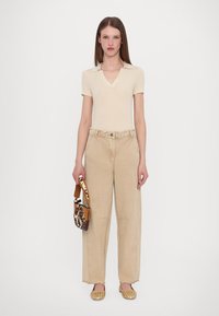 Beige ribbed knit polo shirt, wide beige trousers with frayed hem, woven gold flats, and a handbag with a brown and white pattern.