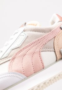 Baskets Puma avec un mélange de daim et de cuir en rose, beige et blanc, présentant une surface texturée, une languette rembourrée et une fermeture à lacets.