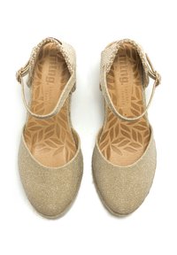 Zapatos de espadrilles en tono dorado con parte superior de tela texturizada, correa al tobillo y plantilla de cuero con un patrón de hojas. Diseño de punta redonda.
