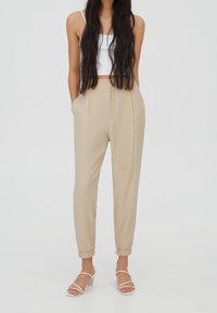 Beige tapschoenen met elastische boorden en zijzakken, gemaakt van lichtgewicht stof. Gecombineerd met witte sandalen met bandjes en een witte top.