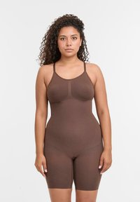 Body marrone con spalline regolabili, texture morbida, design aderente e lunghezza fino a metà coscia. Costruzione senza cuciture con sottili dettagli di contorno.