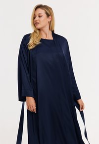 Robe en satin bleu marine à manches longues, coupe droite, avec des liens à la taille. Texture lisse avec un léger éclat.