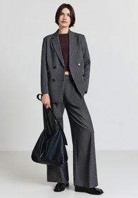 Blazer grigio doppiopetto e pantaloni a gamba larga in tessuto strutturato, abbinati a un top corto in maglia scura e una borsa a tracolla in pelle nera.