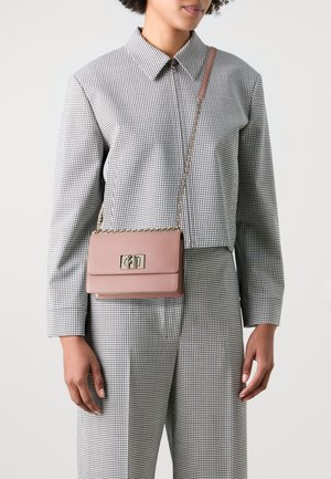 Borsa a tracolla in pelle rosa con hardware dorato, forma rettangolare e tracolla a catena. Indossata da una persona con un outfit a quadri.