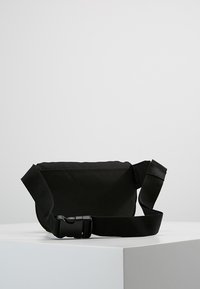 Black nylon crossbody bag with adjustable strap and plastic buckle, featuring a simple rectangular shape and minimal design.