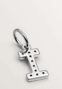 Colgante de letra "I" en metal plateado con perforaciones, suspendido de un aro redondo. Superficie brillante y reflectante con un acabado suave.