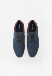 Navy blue canvas shoes with brown leather accents, round toe, and lace-up design. White rubber soles and textured upper detail.