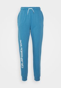 Blue sweatpants made of soft cotton, with an elastic waistband and drawstring. Features side pockets and a large white logo down one leg.