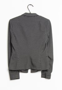 Mustan takki, jossa on pilkullinen kuvio, klassinen kaulus ja pitkät hihat. Sileä kangas, joka istuu vartalolle täydellisesti ja sisältää takana venvin.