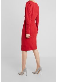 Rotes, figurbetontes Kleid mit langen Ärmeln, einem runden Ausschnitt und sichtbaren Nahtdetails. Kombiniert mit silbernen High Heels.