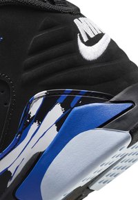 Talons de baskets Nike noirs avec logo blanc brodé, présentant un design abstrait de traits de peinture bleus, blancs et noirs sur la semelle intermédiaire.