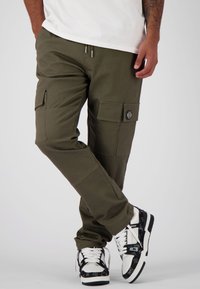 Groene cargo broek met meerdere zakken, elastische tailleband en verstelbare koorden. Gecombineerd met zwart-witte sneakers met een patroon.
