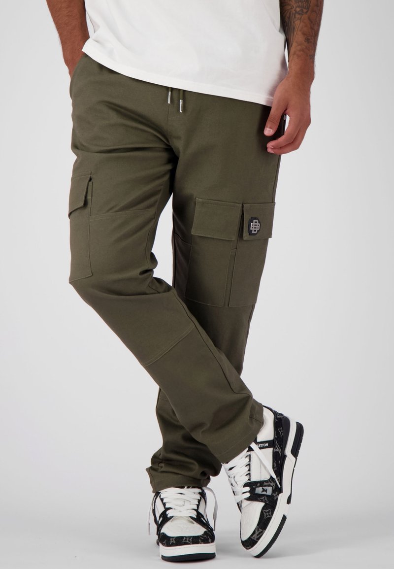 Groene cargo broek met meerdere zakken, elastische tailleband en verstelbare koorden. Gecombineerd met zwart-witte sneakers met een patroon.