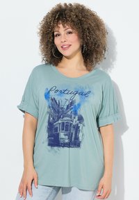 Camiseta oversized de color azul claro con un boceto azul de un tranvía y el texto "Portugal". Mangas cortas con dobladillo y material de algodón suave.
