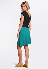 Sort ribbet bluse med V-udskæring og korte ærmer, parret med en teal-skreddersyet nederdel. Gule blokhælede sandaler fuldender outfittet.