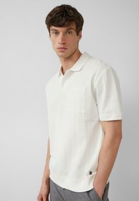 Wit gestreepte polo met korte mouwen, een polo-kraag en een borstzak. Gemaakt van een textuurstof, met een logo op de zoom.