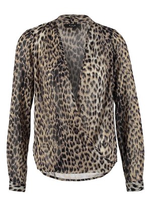 Frau trägt eine Bluse mit Leopardenmuster, schwarze Skinny-Jeans, schwarze High Heels und hält eine schwarze Clutch mit Quasten.