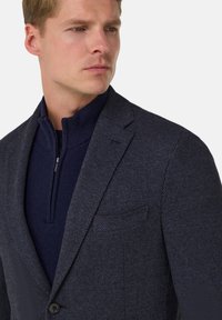 Námořnicky modré sako se vzorem rybí kosti, vyrobené z texturované látky, s klopovým límcem se zářezem a zapínáním na jeden knoflík.