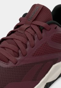 Bordeauxrød sportssko med mesh og syntetiske overlæg, teksturerede snørebånd og gummisål. Har Reebok-logo på tungen.