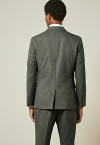 Veste de costume grise vue de dos, présentant un tissu texturé, une fente unique et des poignets boutonnés, assortie à un pantalon coordonné.