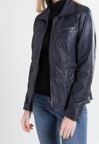 Mörkblå läderjacka med dragkedja framtill, två sidofickor och en bröstficka. Har en slät textur och subtila sömnadsdetaljer.