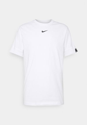 Biała koszulka Nike z krótkim rękawem, z czarnym logo w kształcie łyżwy umieszczonym centralnie poniżej linii szyi oraz czarnym napisem "NIKE" na mankiecie lewego rękawa.
