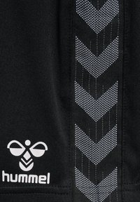 Zwarte stof met wit hummel-logo en verticale reflecterende chevron-patroonstrip genaaid aan de zijkant.