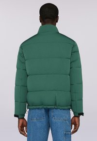 Zelená péřová bunda s vysokým límcem, horizontálně prošívaným designem a elastickými manžetami. Tkanina vypadá hladce a matně.