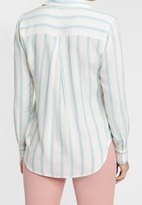 White button-up shirt with light blue vertical stripes, curved hem, and long sleeves. Textured fabric with back yoke detailing.